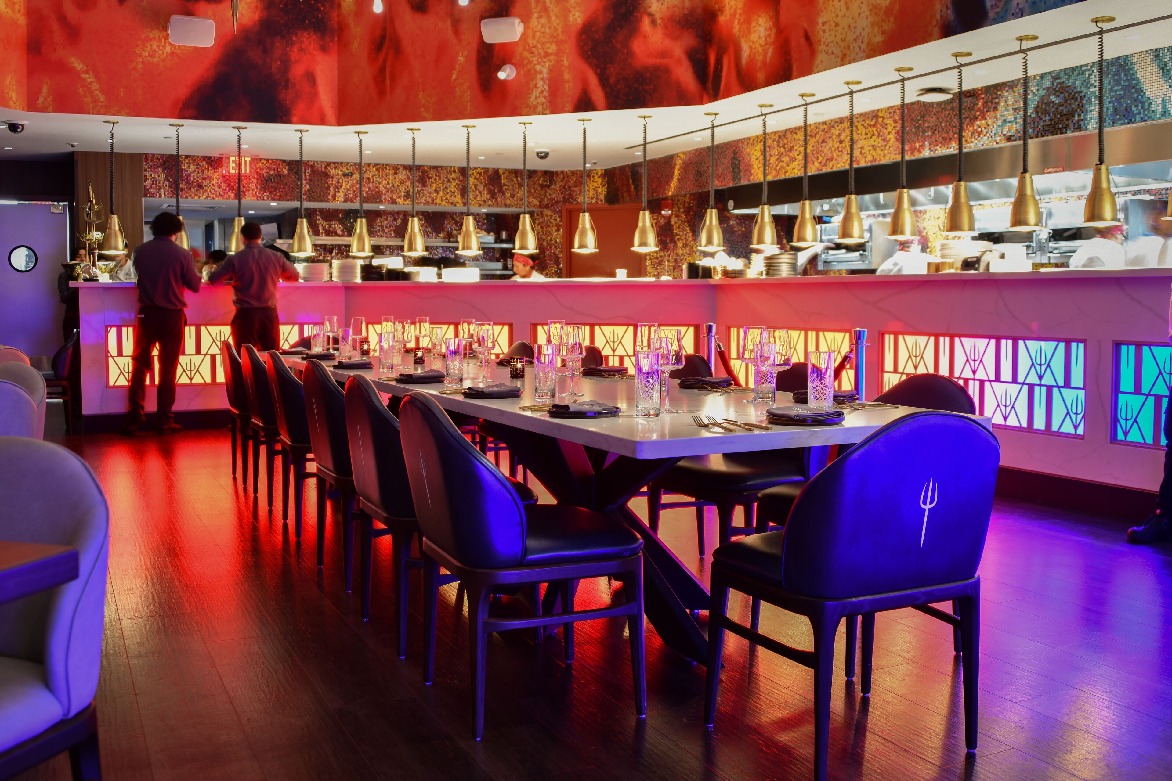 A restaurant with a long counter, multiple hanging lights, and a modern interior design.