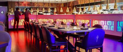 A restaurant with a long counter, multiple hanging lights, and a modern interior design.