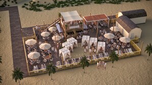 A beachside resort with outdoor seating, umbrellas, and a bar area.