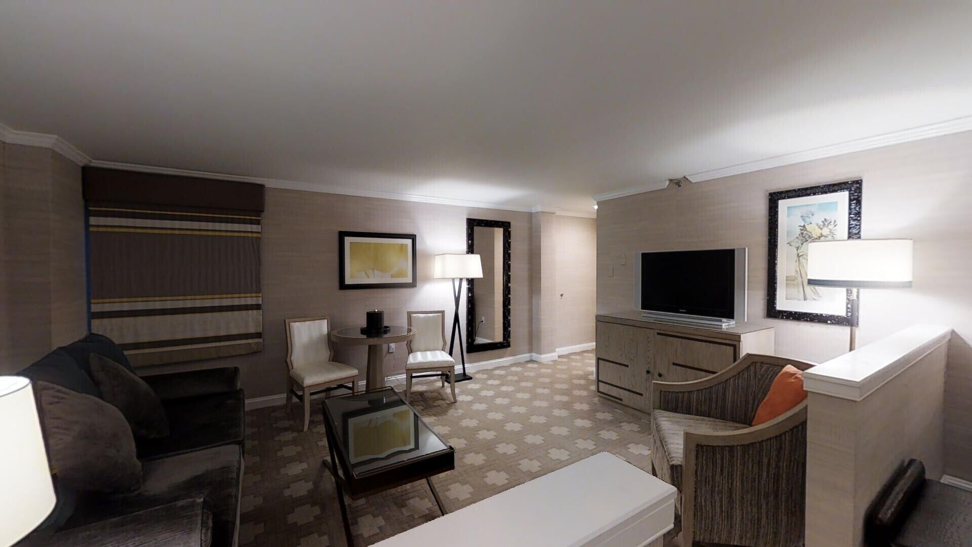 Une chambre d’hôtel équipée d’un canapé, d’un fauteuil, d’une télévision, d’un bureau, d’une lampe et d’un tapis à motifs.