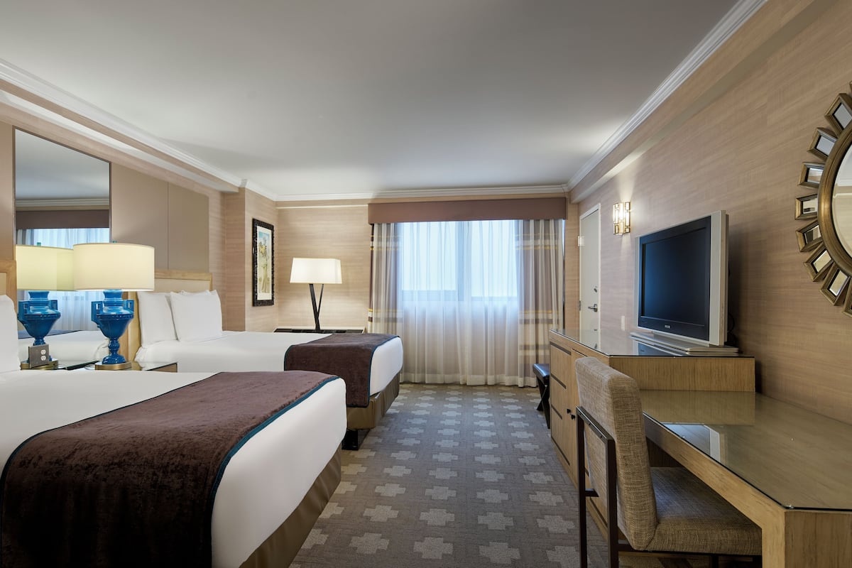 Ein Hotelzimmer mit zwei Betten, einem Schreibtisch, einem Fernseher und einem großen Spiegel.