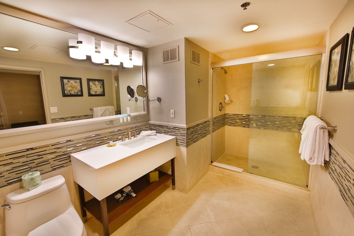 A modern bathroom with a large mirror, a white sink, a glass-enclosed shower, and a toilet.