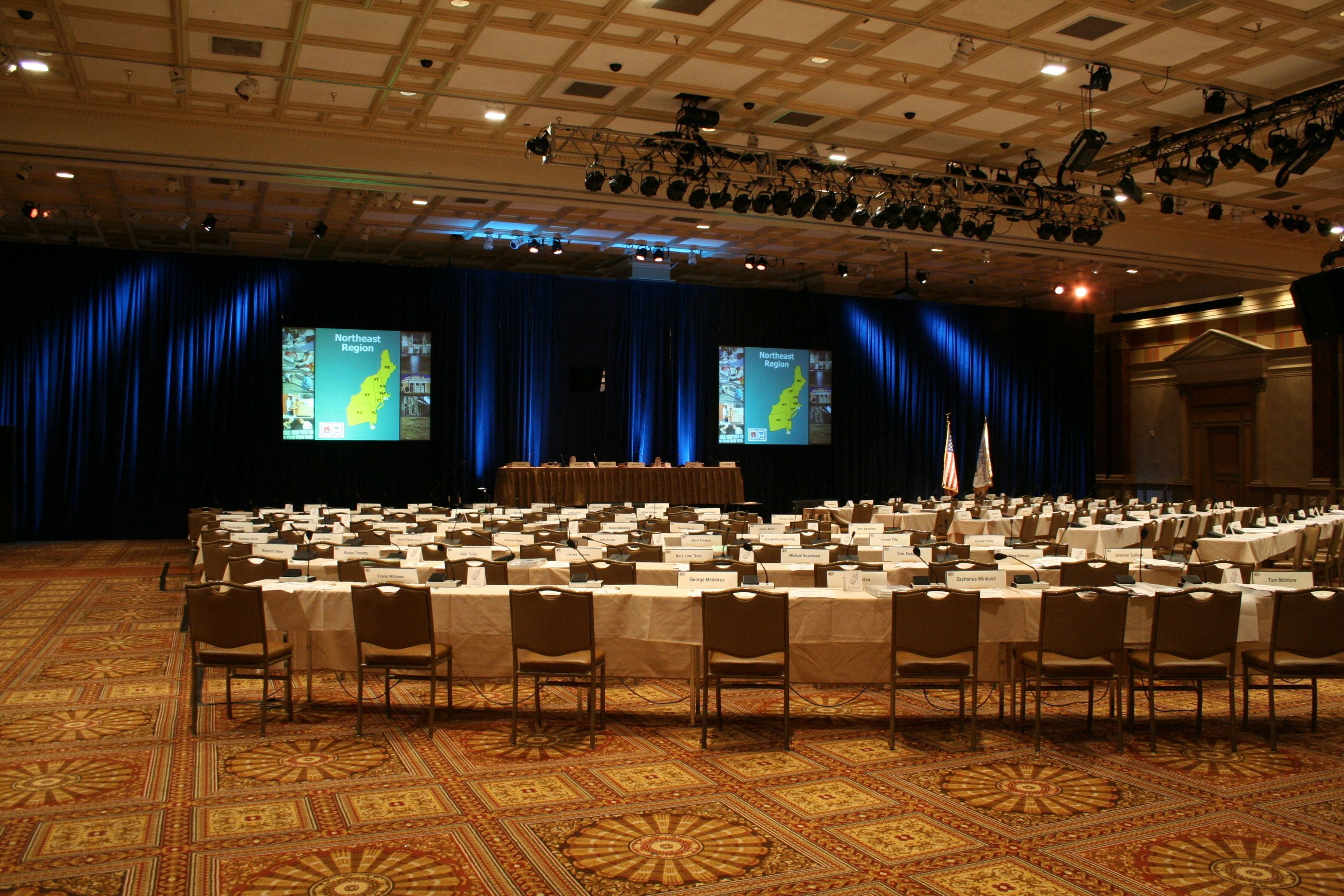 A conference room with a long table, chairs, a podium, and two screens displaying a map.