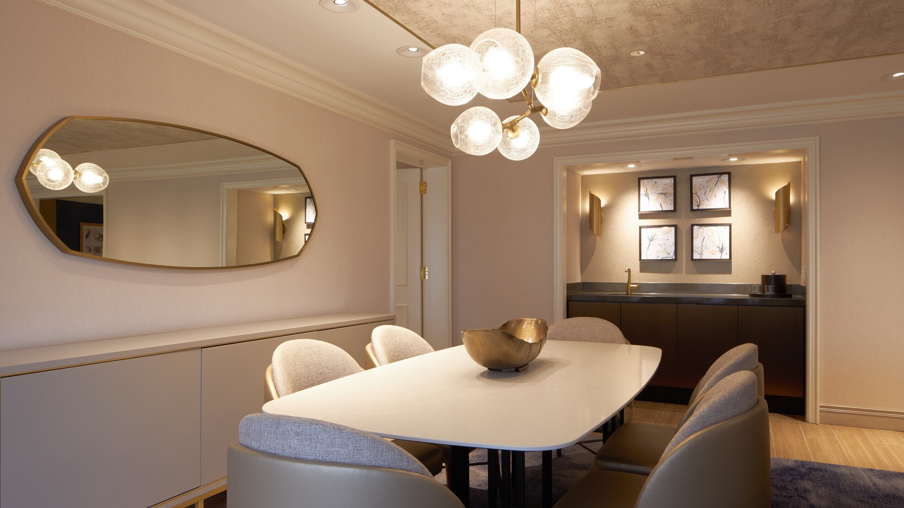 Een eetruimte met een ronde tafel, stoelen, een grote spiegel en een kroonluchter.