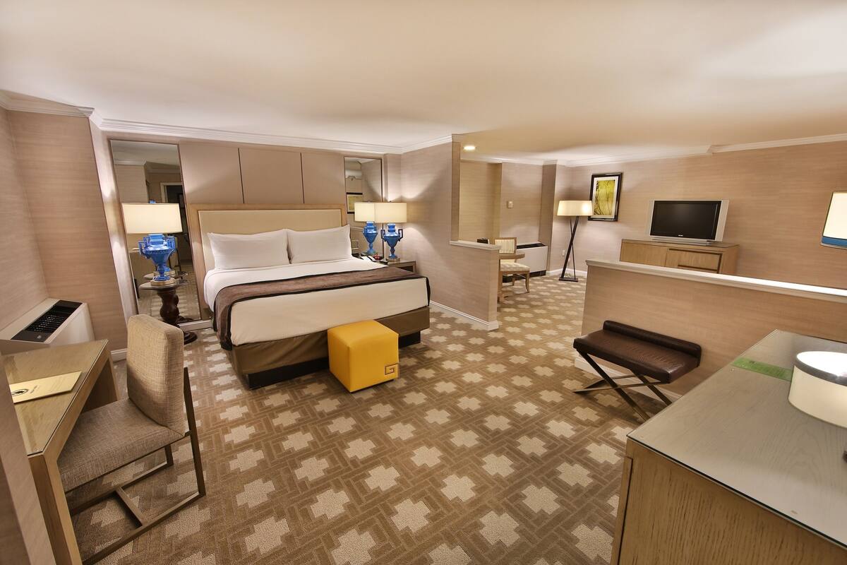 Ein Hotelzimmer mit Bett, Nachttisch, Sessel, Schreibtisch, Fernseher und einem kleinen Hocker.