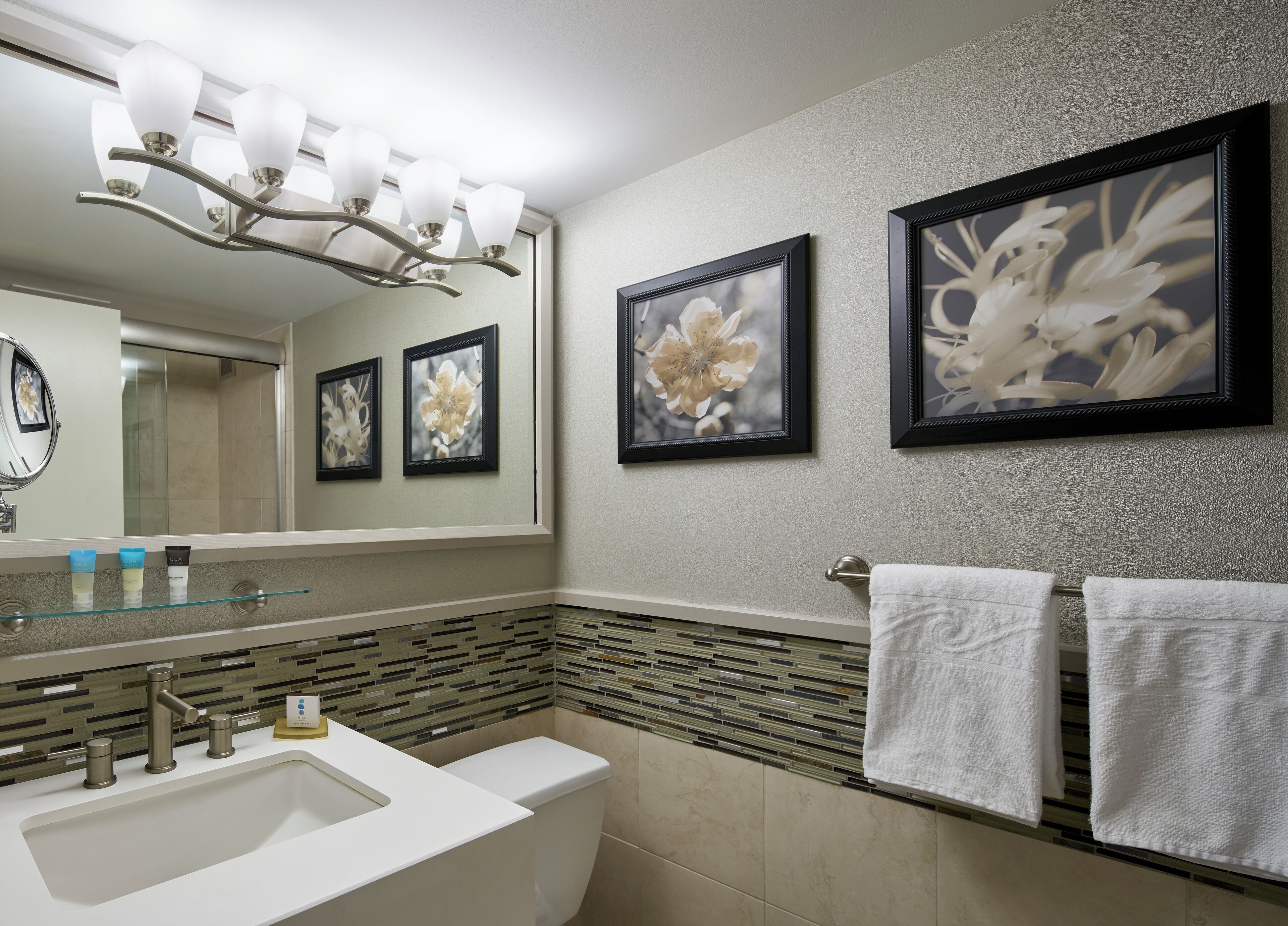 A bathroom with a large mirror, a sink, a toilet, and framed floral artwork on the wall.