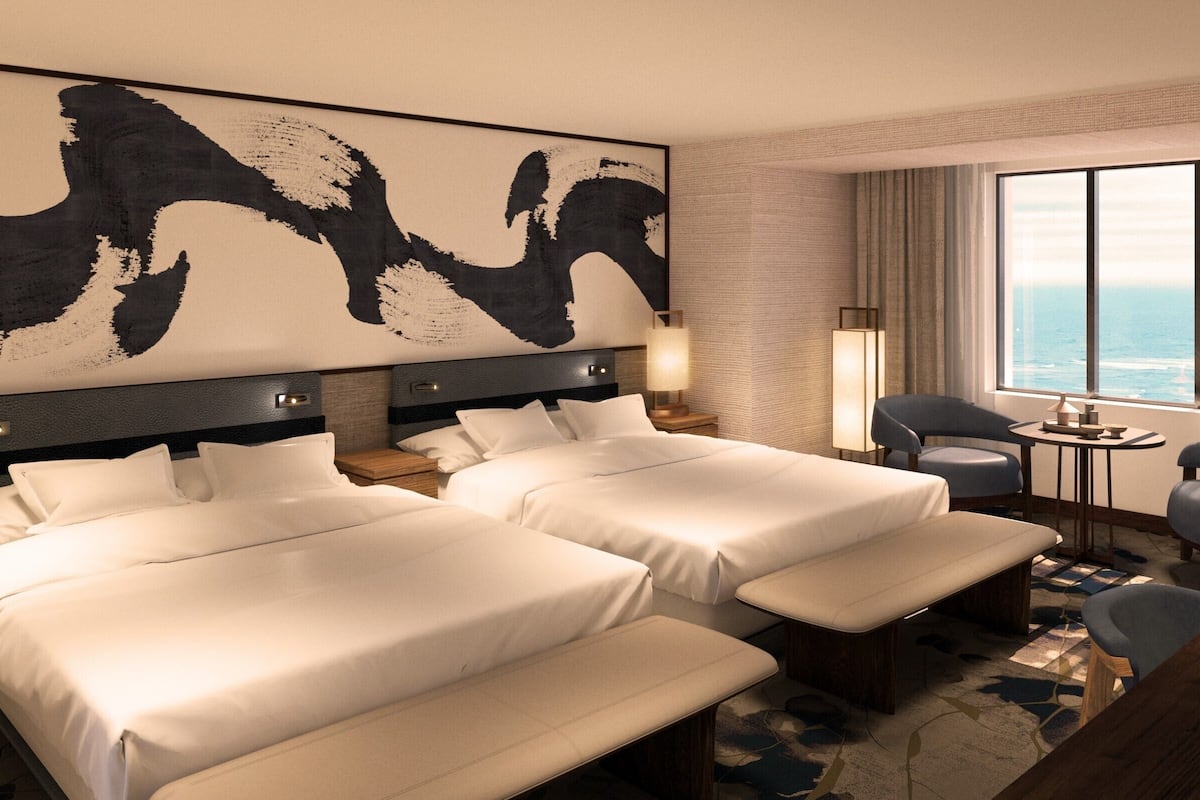 Ein Hotelzimmer mit zwei Betten, einem großen abstrakten Gemälde, Meerblick und einem kleinen Tisch mit Stühlen.