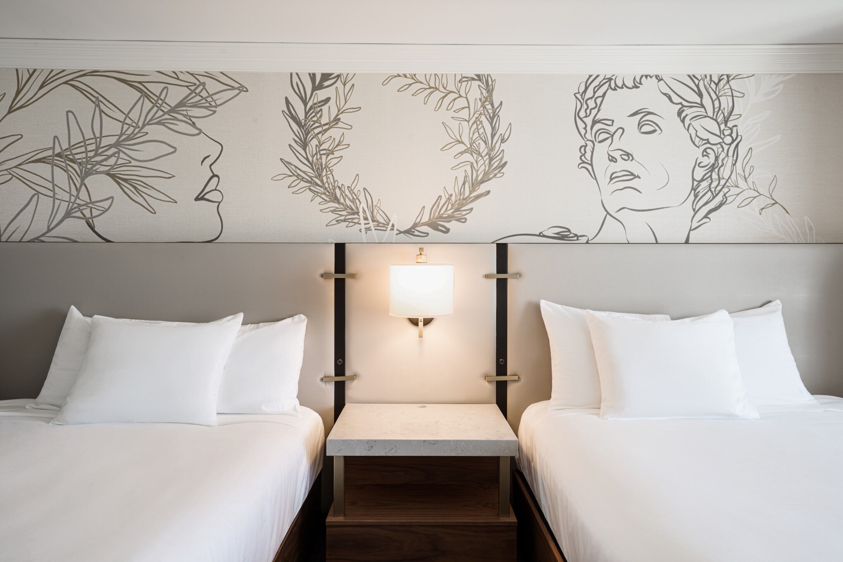 Une chambre d’hôtel avec deux lits, une table de chevet et un mur orné de dessins linéaires artistiques.
