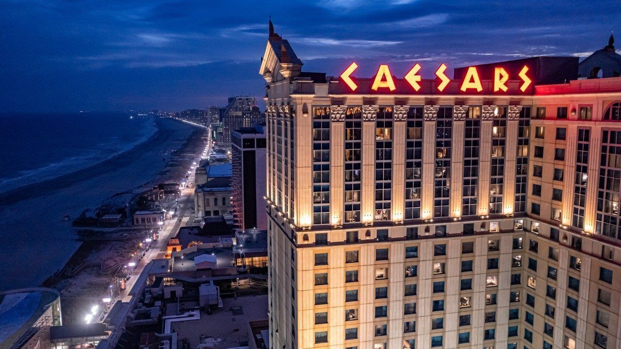 A high-rise hotel with a prominent 'Caesars' sign, a beachfront location, and a city skyline in the background.