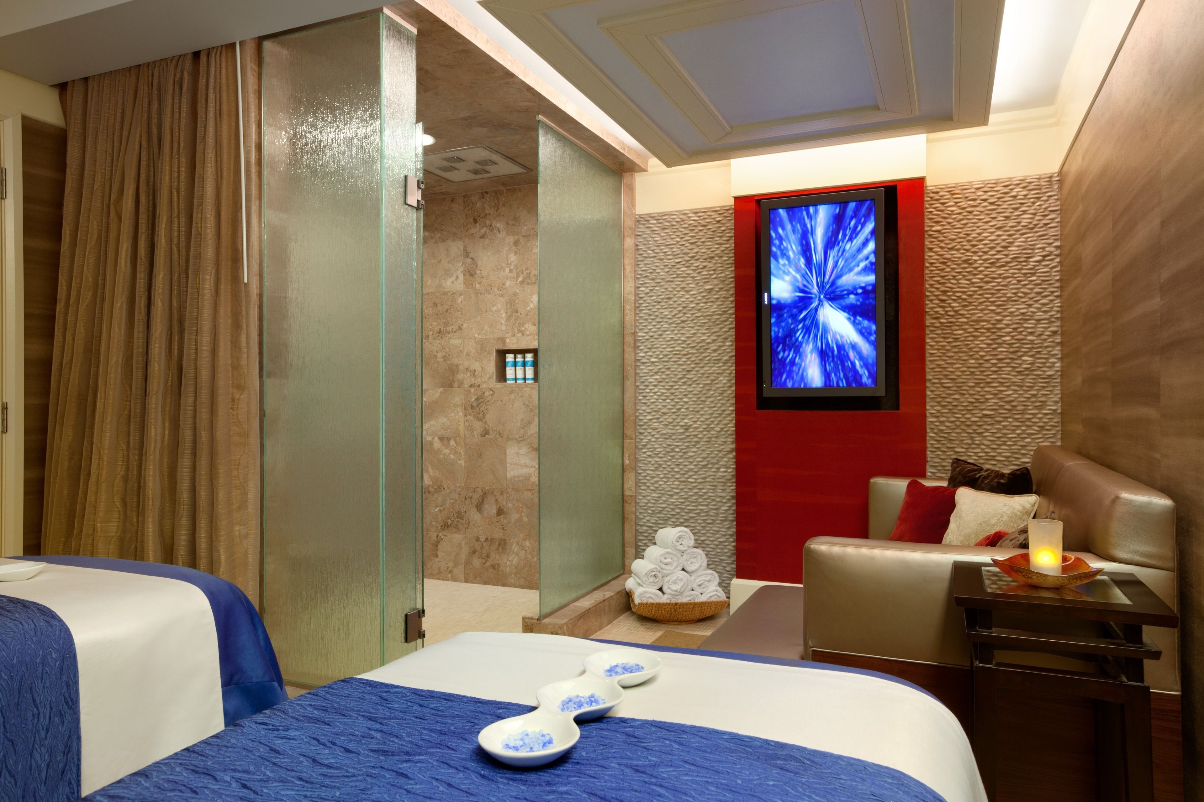 Una camera d'albergo con due letti, una TV, un lettino da massaggio e una piccola zona relax.