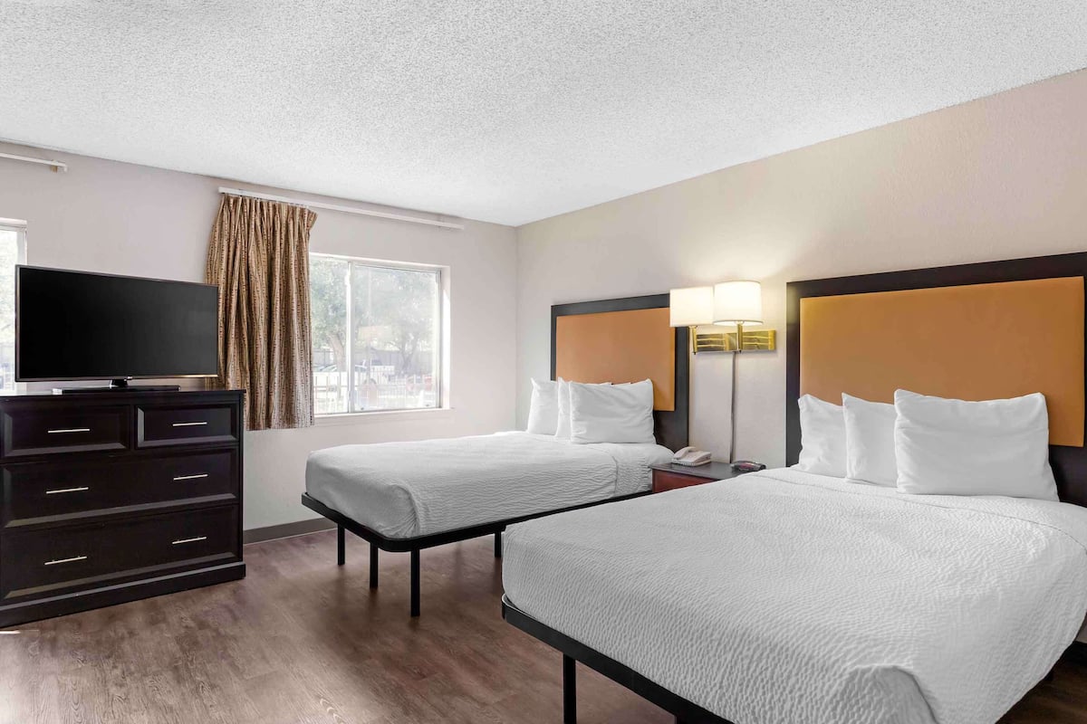 A hotel room with two beds, a TV, a dresser, and a window with curtains.