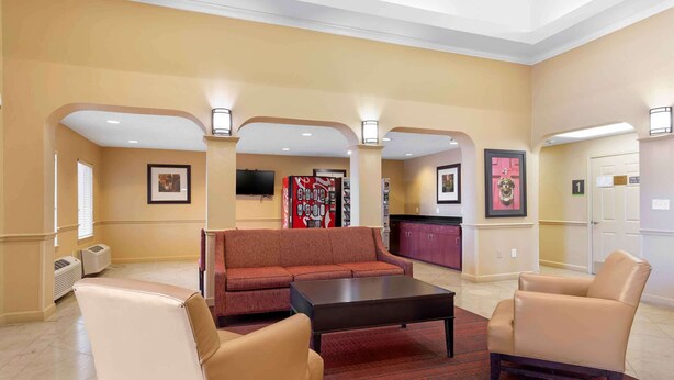 A hotel lobby with a red sofa, beige armchairs, a coffee table, and a Coca-Cola refrigerator. - Extended Stay America Suites Houston Katy Freeway Energy Cor (Houston)