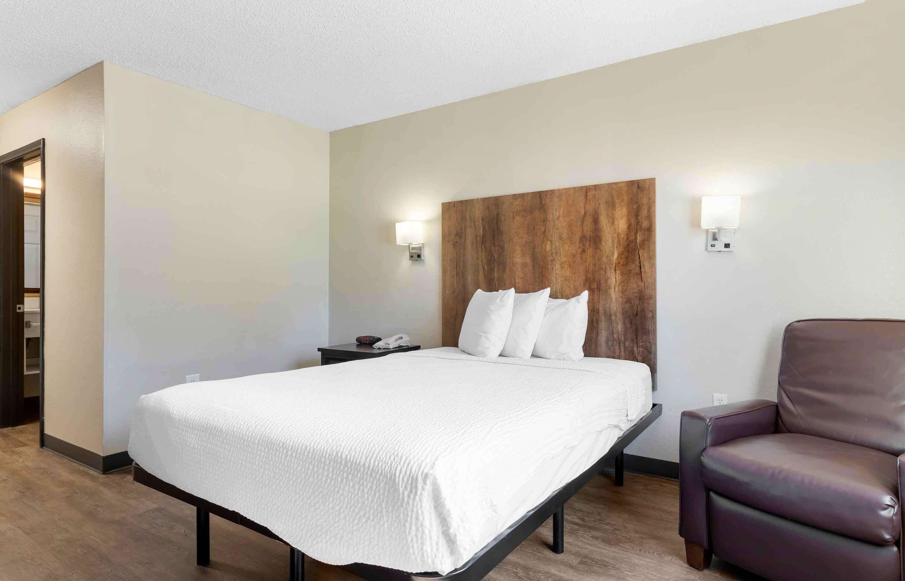 A hotel room with a bed, a chair, a nightstand, and a wooden headboard.