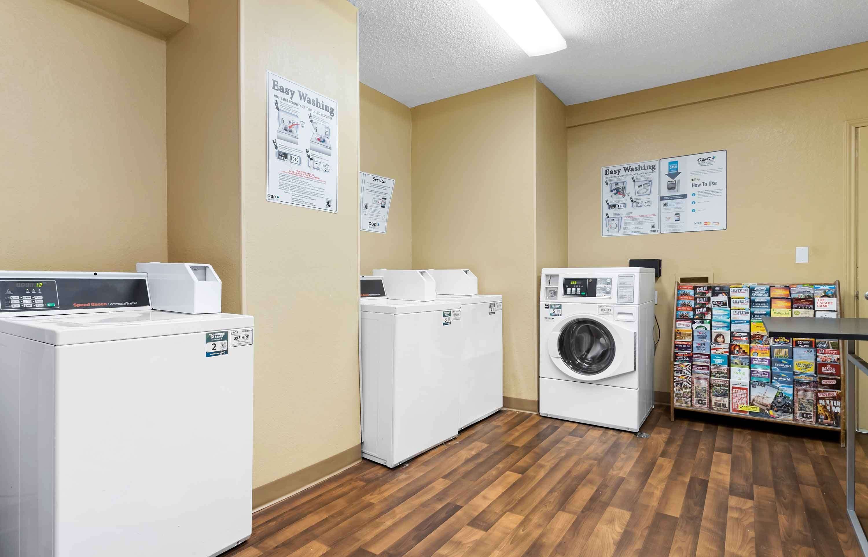 A laundry room with three washers and dryers, wooden flooring, and informational posters on the walls.