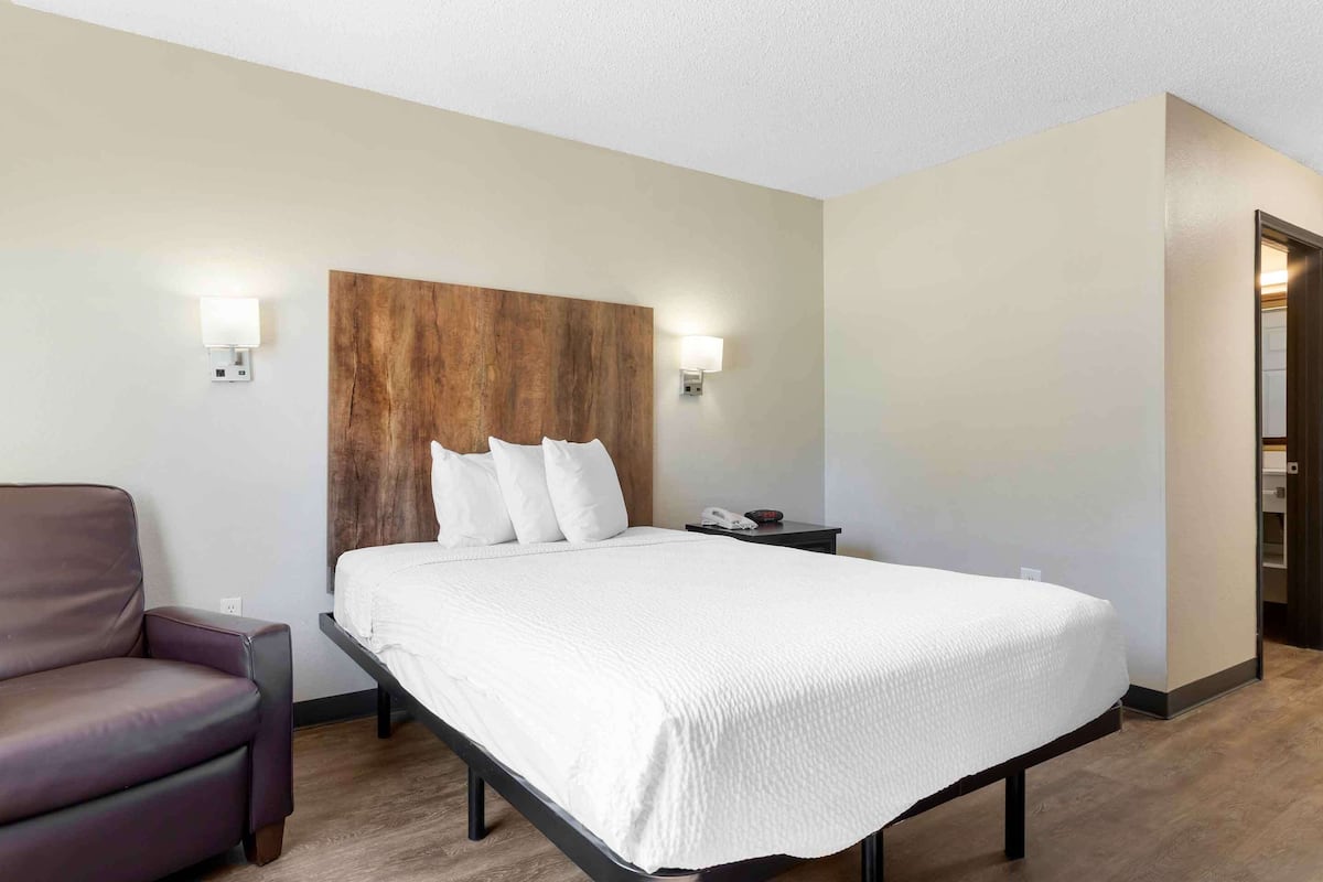 A hotel room with a bed, a chair, a nightstand, and a wooden headboard.