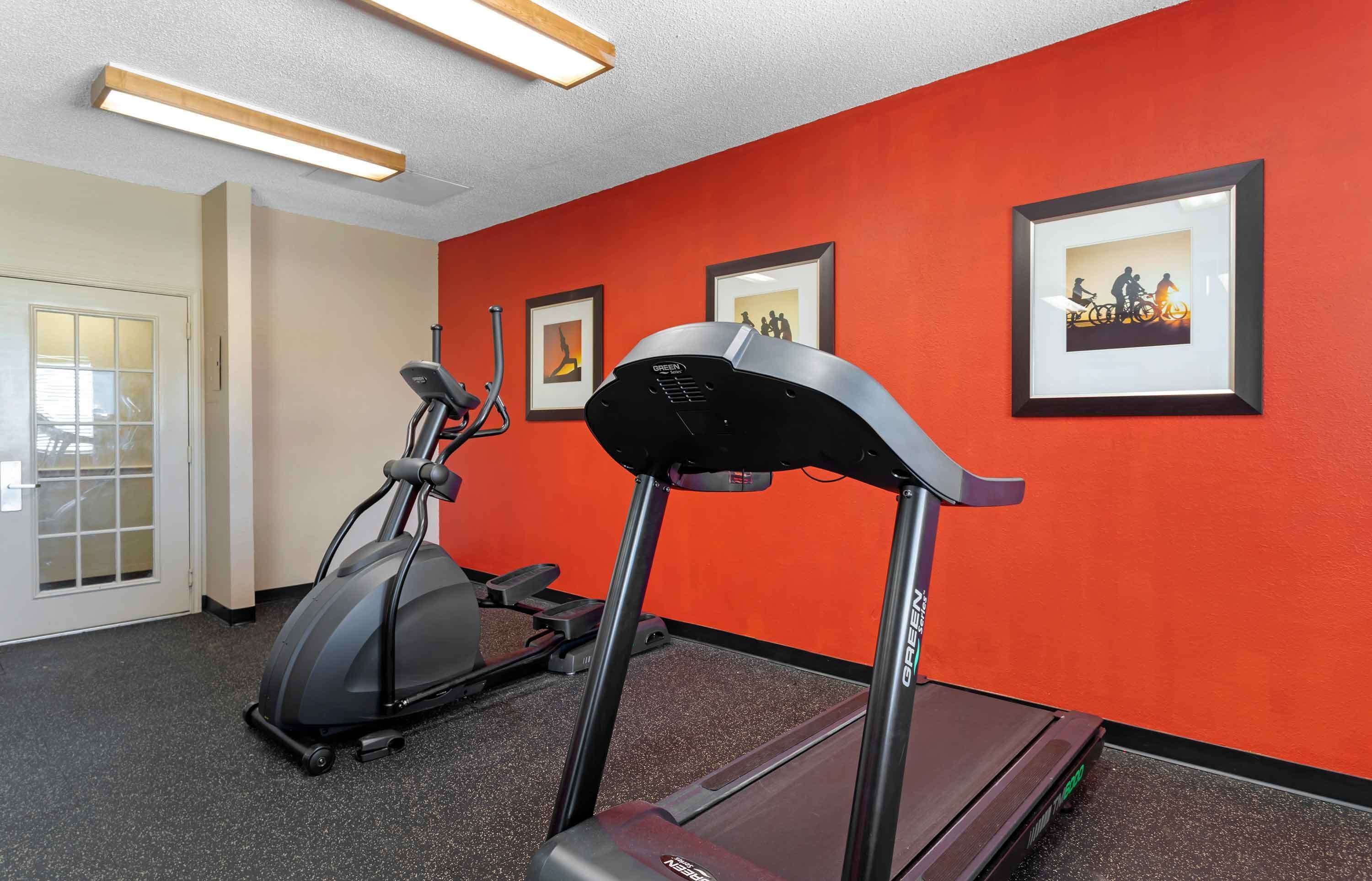 Une salle de sport équipée de tapis de course et d’un appareil elliptique, avec des murs rouges et des œuvres d’art encadrées.