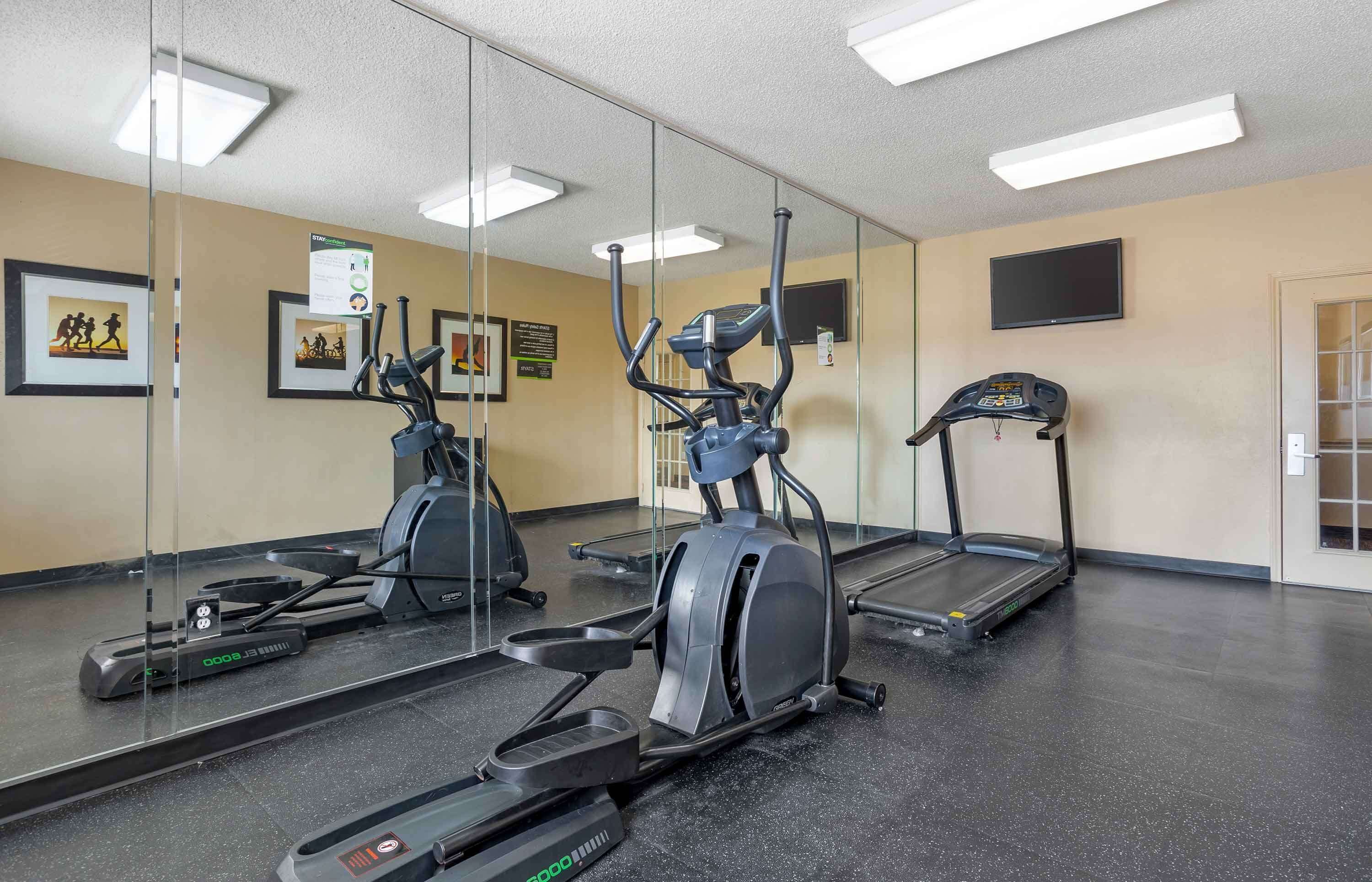 A gym with exercise equipment, a mirror, and a television on the wall.