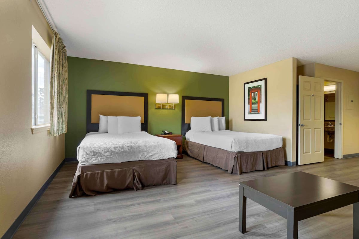 A hotel room with two beds, a small table, and a door leading to another room.