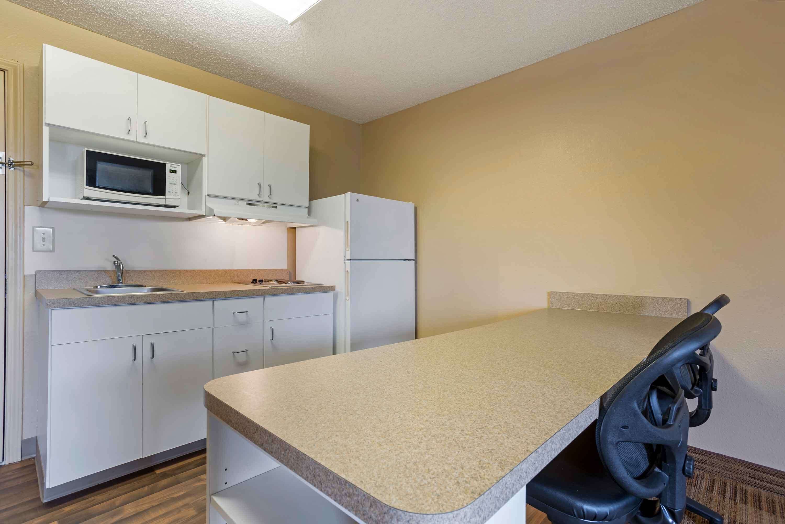 A compact kitchen with white cabinets, a microwave, a refrigerator, and a small countertop.