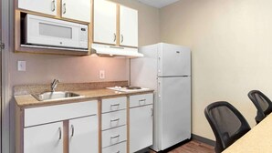 A compact kitchen with white cabinetry, a microwave, a refrigerator, a sink, and a dining area with two chairs. - Extended Stay America Select Suites - Houston - Sugar Land (Sugar Land)