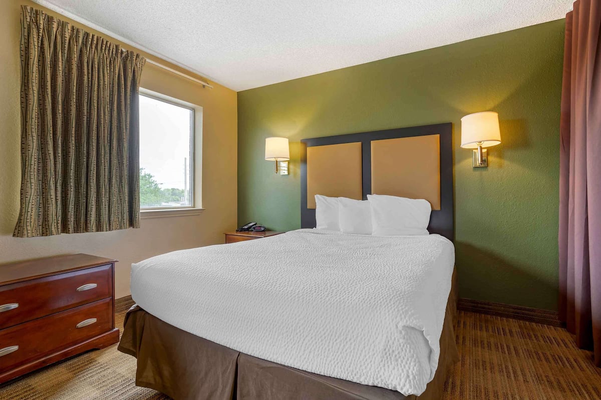 A hotel room with a large bed, two bedside lamps, a wooden dresser, and a window with curtains.