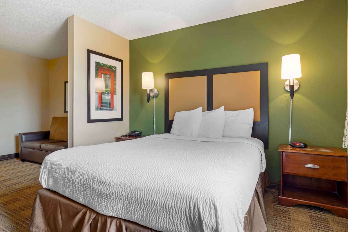 A hotel room with a large bed, two bedside tables, a nightstand, a chair, and a framed picture on the wall.