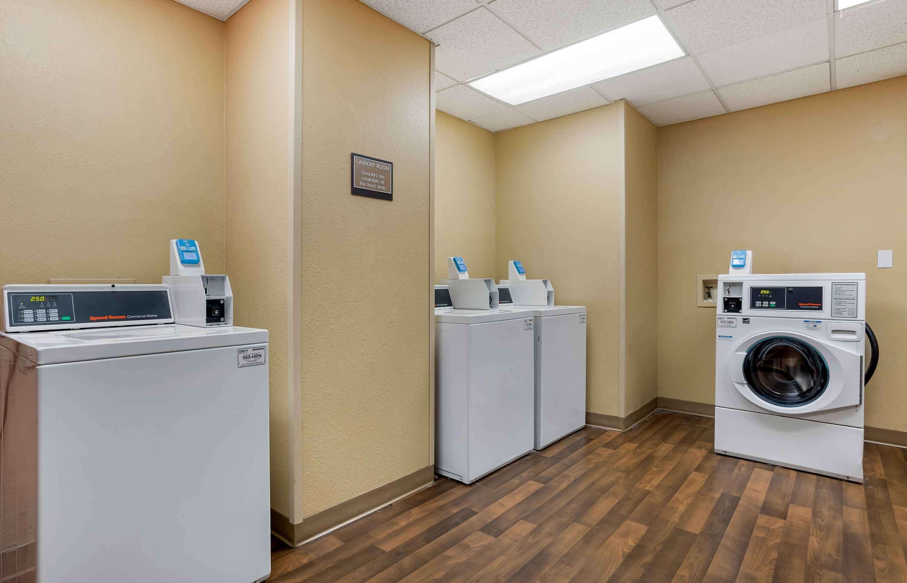 A laundry room with a front-loading washer and dryer, two wall-mounted dryers, and a sign indicating the room's purpose.