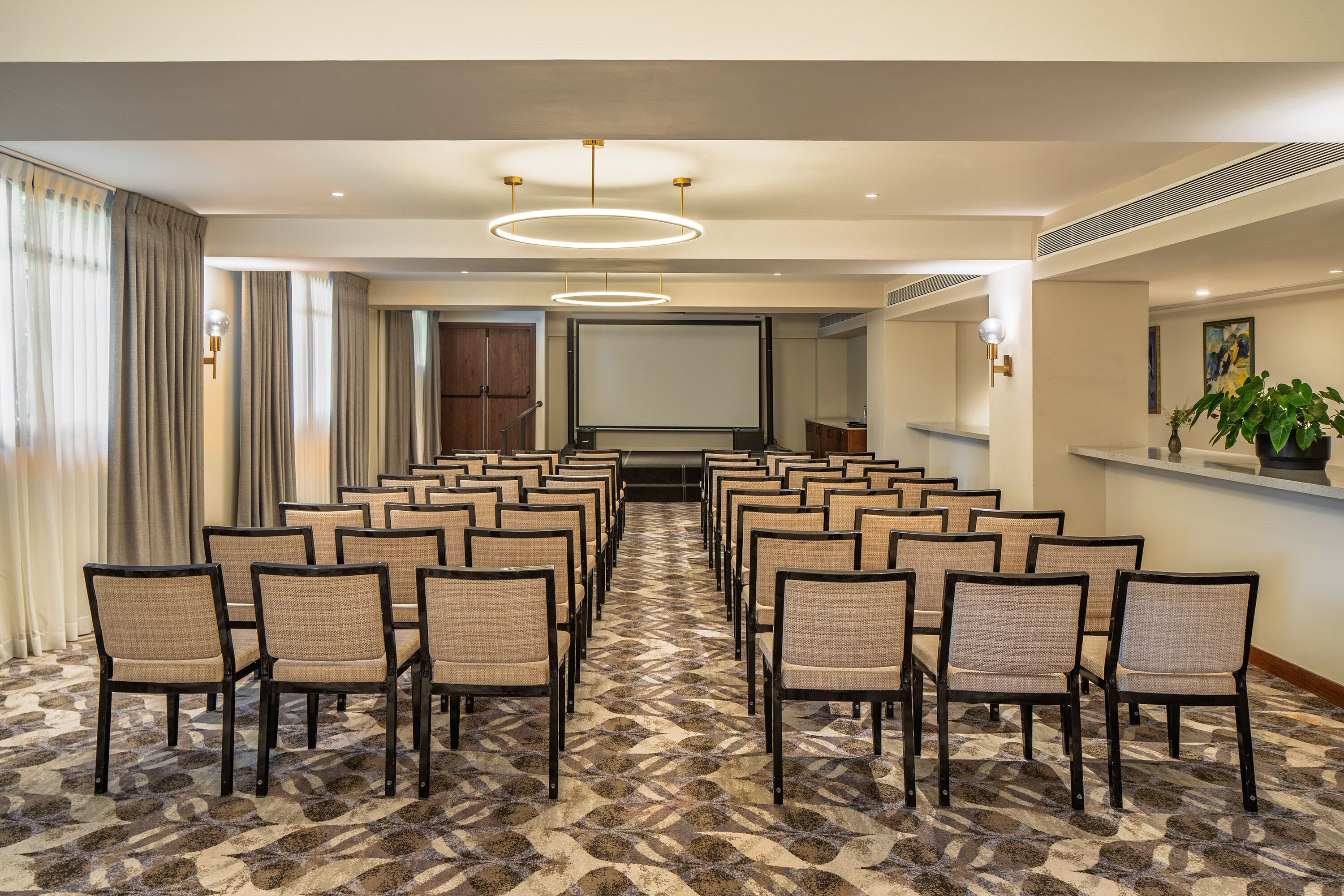 Une salle de conférence avec des rangées de chaises, un grand écran et une moquette à motifs.