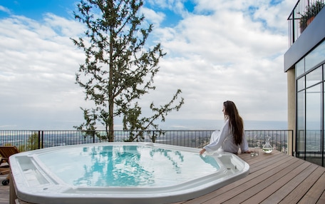 A hot tub on a wooden deck with a view of the ocean and a tree.