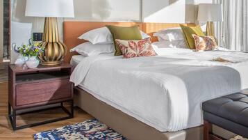 Una habitación de hotel moderna con una cama grande, dos mesitas de noche con lámparas, una mesita auxiliar con un florero y una alfombra estampada.