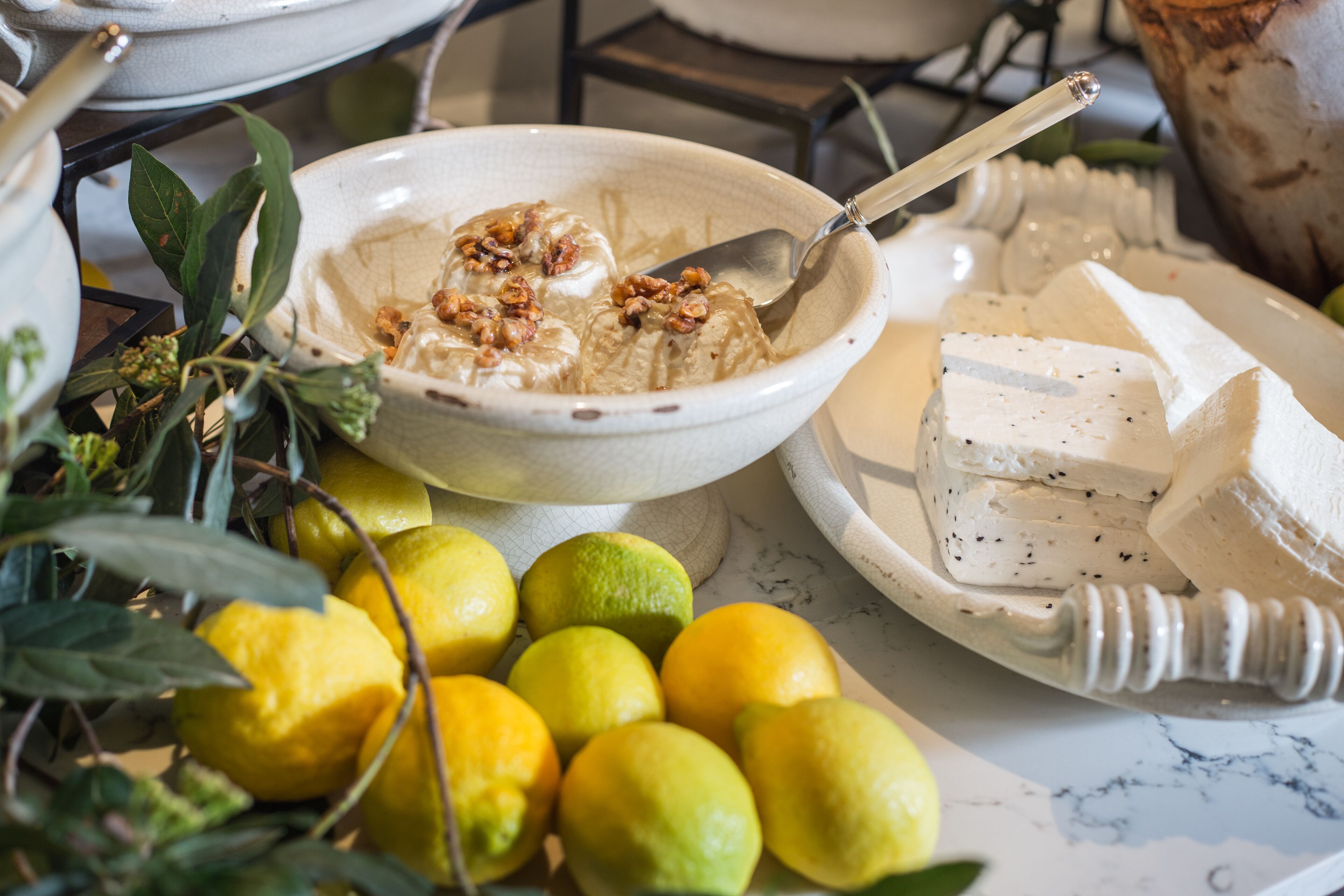 Un bol de nourriture avec une cuillère, une assiette de fromage et des citrons sur une table.