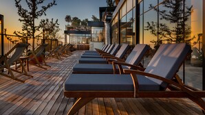 Una terrazza con lettini e un edificio con ampie finestre che riflettono alberi.