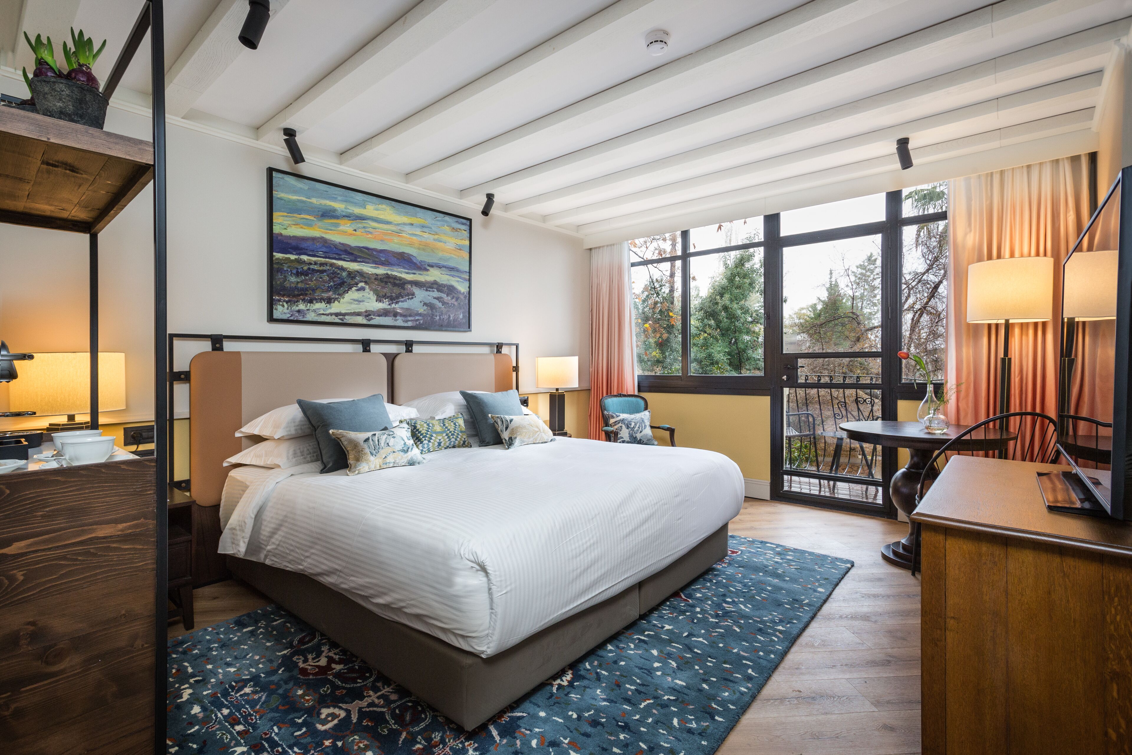 A modern bedroom with a large bed, a desk, and a view of the outdoors.