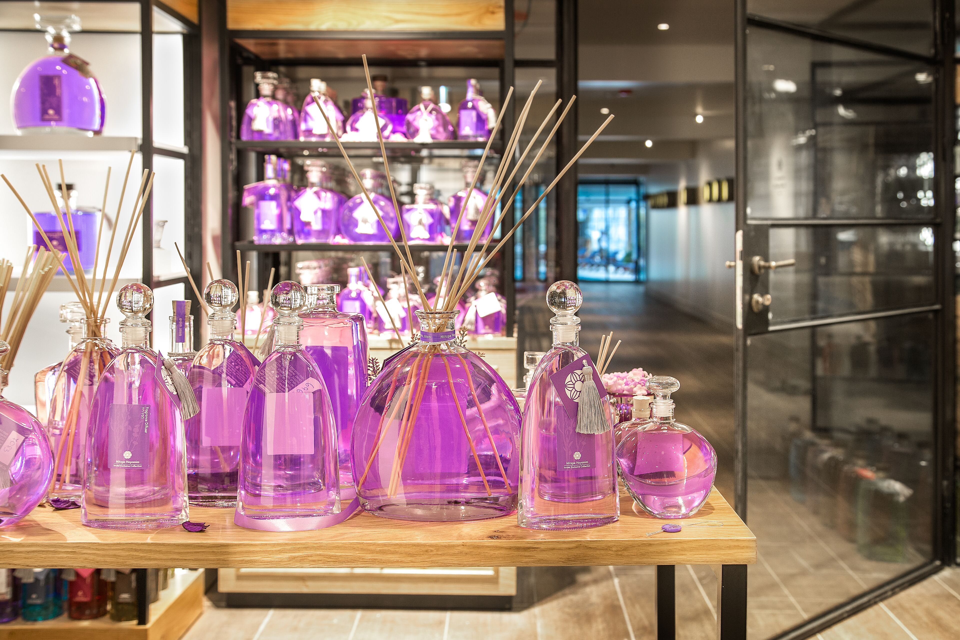 Een presentatie van paarse glazen flessen met houten stokjes, waarschijnlijk voor parfum, in een winkel met schappen op de achtergrond.