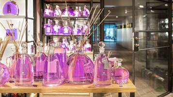 Een presentatie van paarse glazen flessen met houten stokjes, waarschijnlijk voor parfum, in een winkel met schappen op de achtergrond.