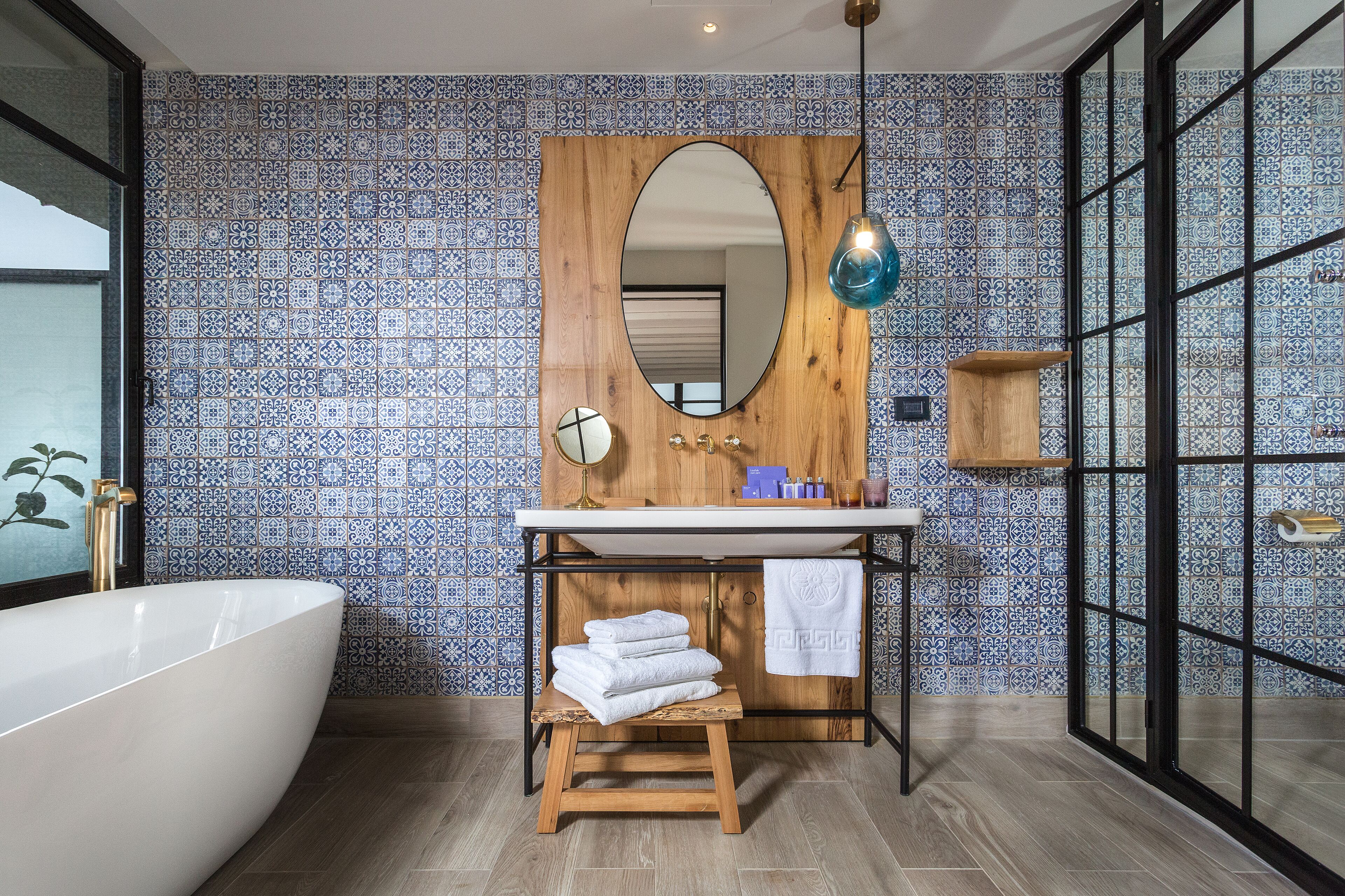 Ein Badezimmer mit einer freistehenden Badewanne, einem hölzernen Waschtisch mit Spiegel und einer gefliesten Rückwand.