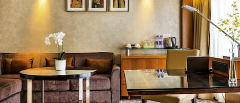 Una habitación de hotel moderna con sofá, una mesa redonda, una mesita de cristal y un escritorio con una computadora portátil, además de un jarrón decorativo.