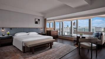 A modern hotel room with a large bed, a desk, a sofa, and a view of the city.