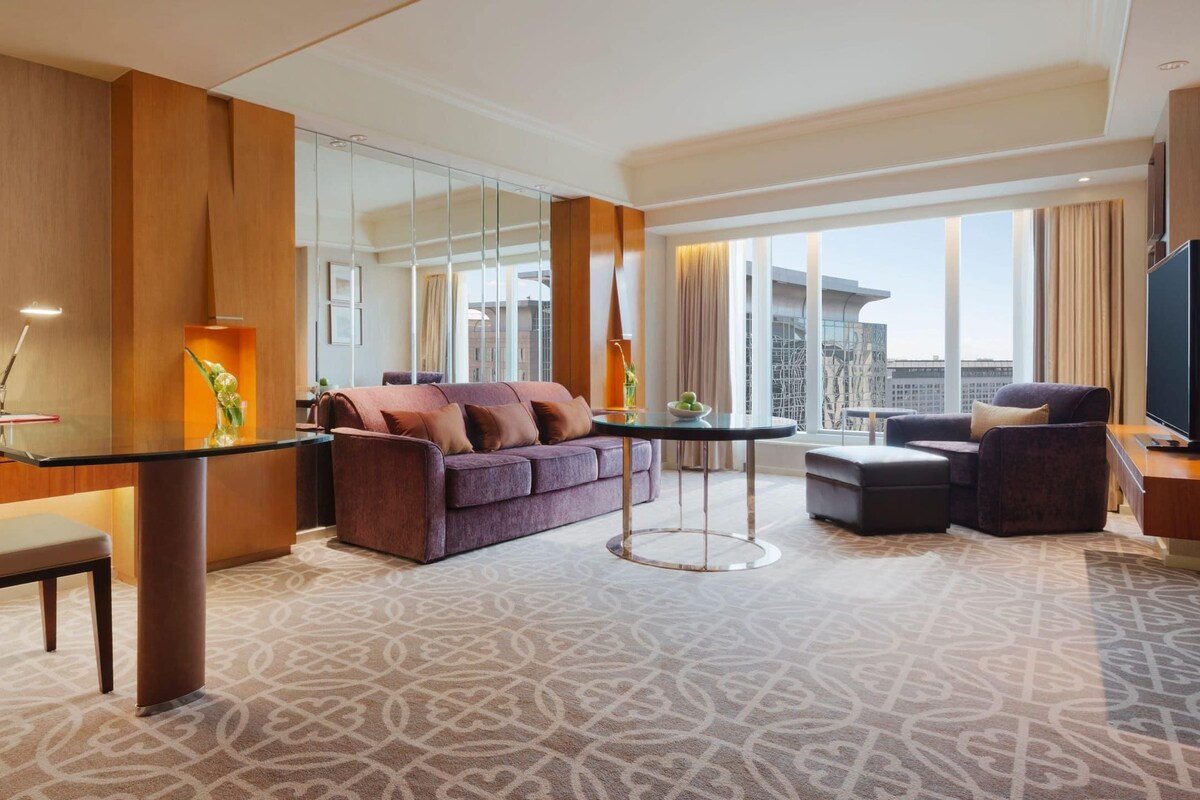 A hotel room with a glass dining table, a sofa, a chair, and a TV.