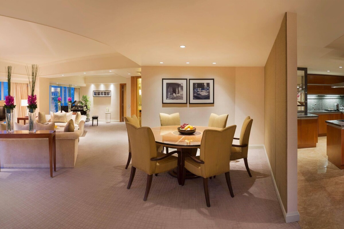 A modern dining area with a round table, chairs, and a fruit bowl.