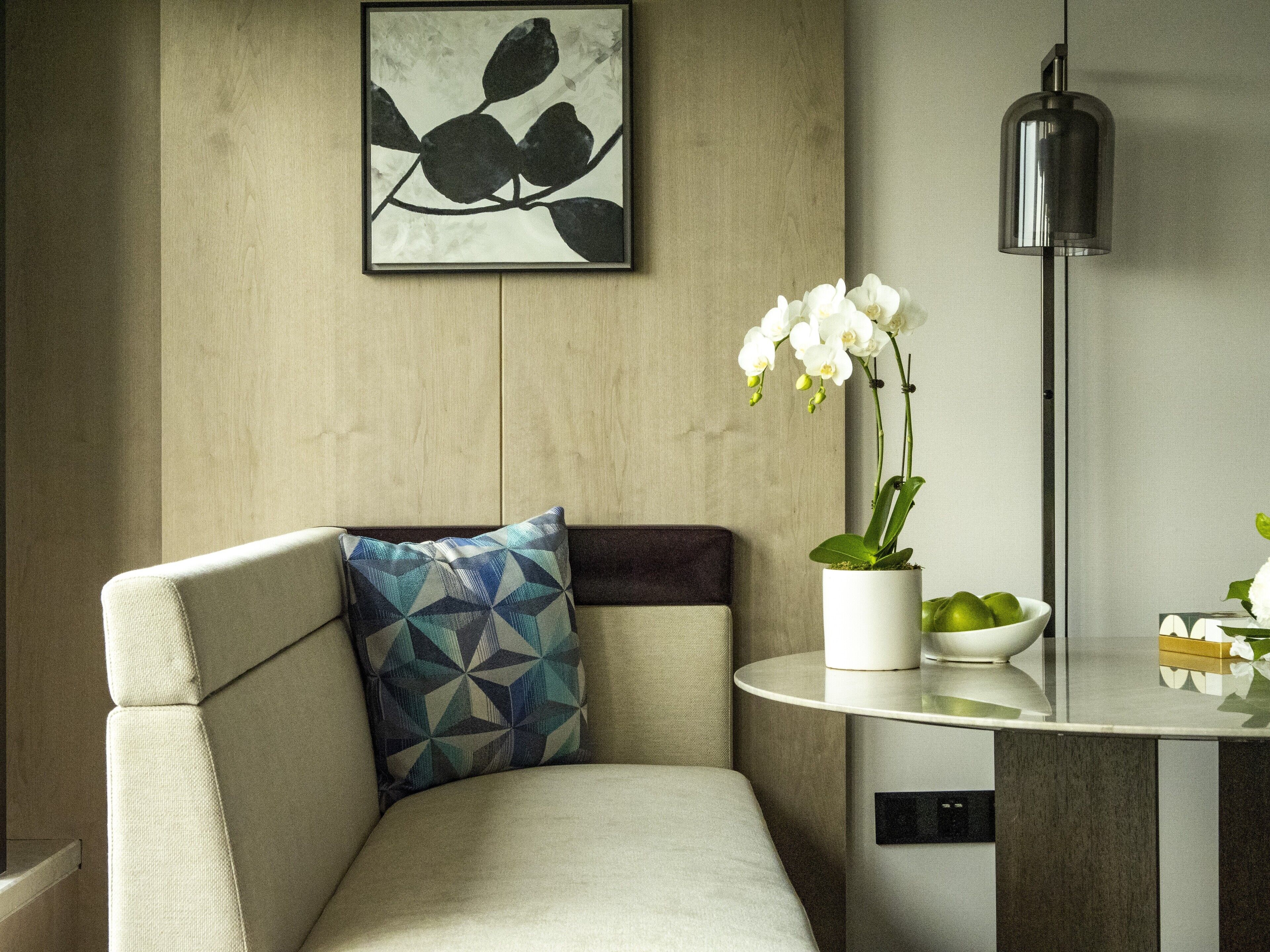 A modern living room with a sofa, a geometric patterned pillow, a white vase with an orchid, and a minimalist lamp.