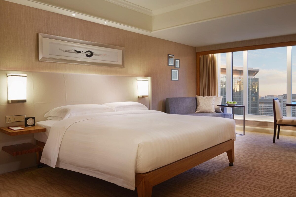 A hotel room with a large bed, a desk, a chair, and a city view.