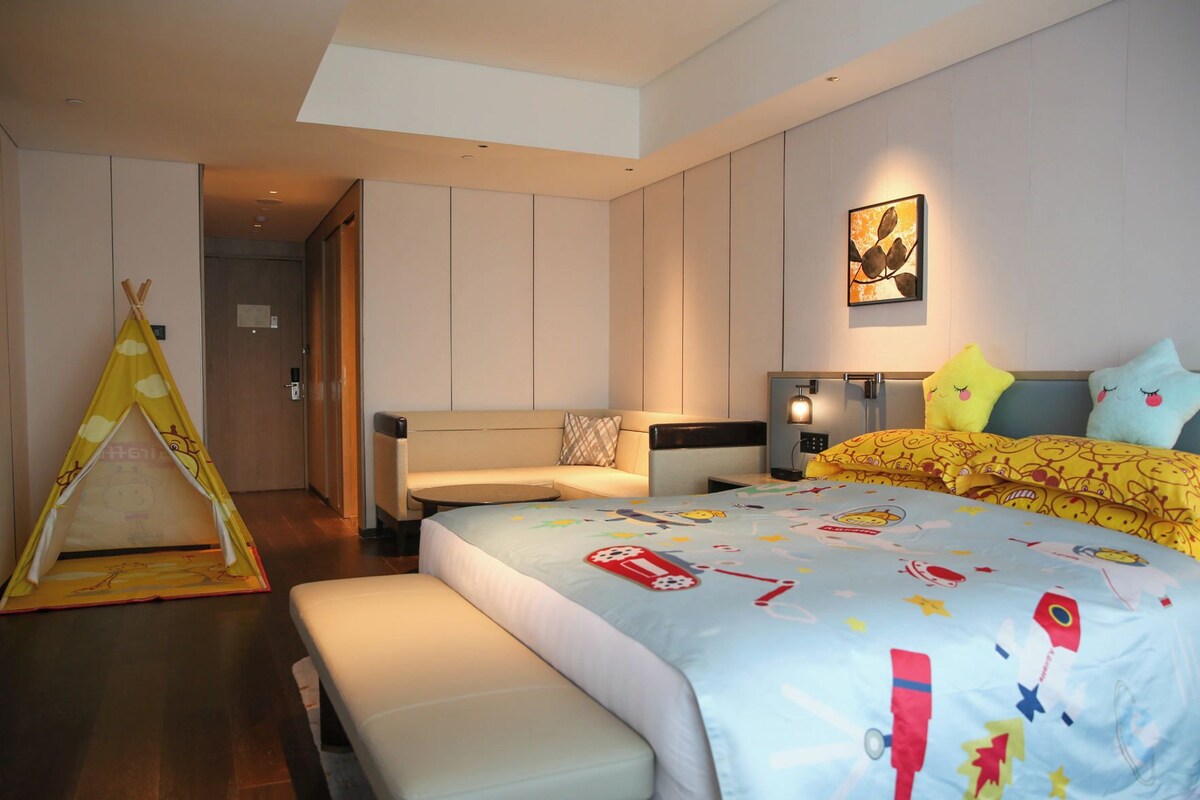 A modern hotel room with a bed, a sofa, a small table, and a tent-like structure.