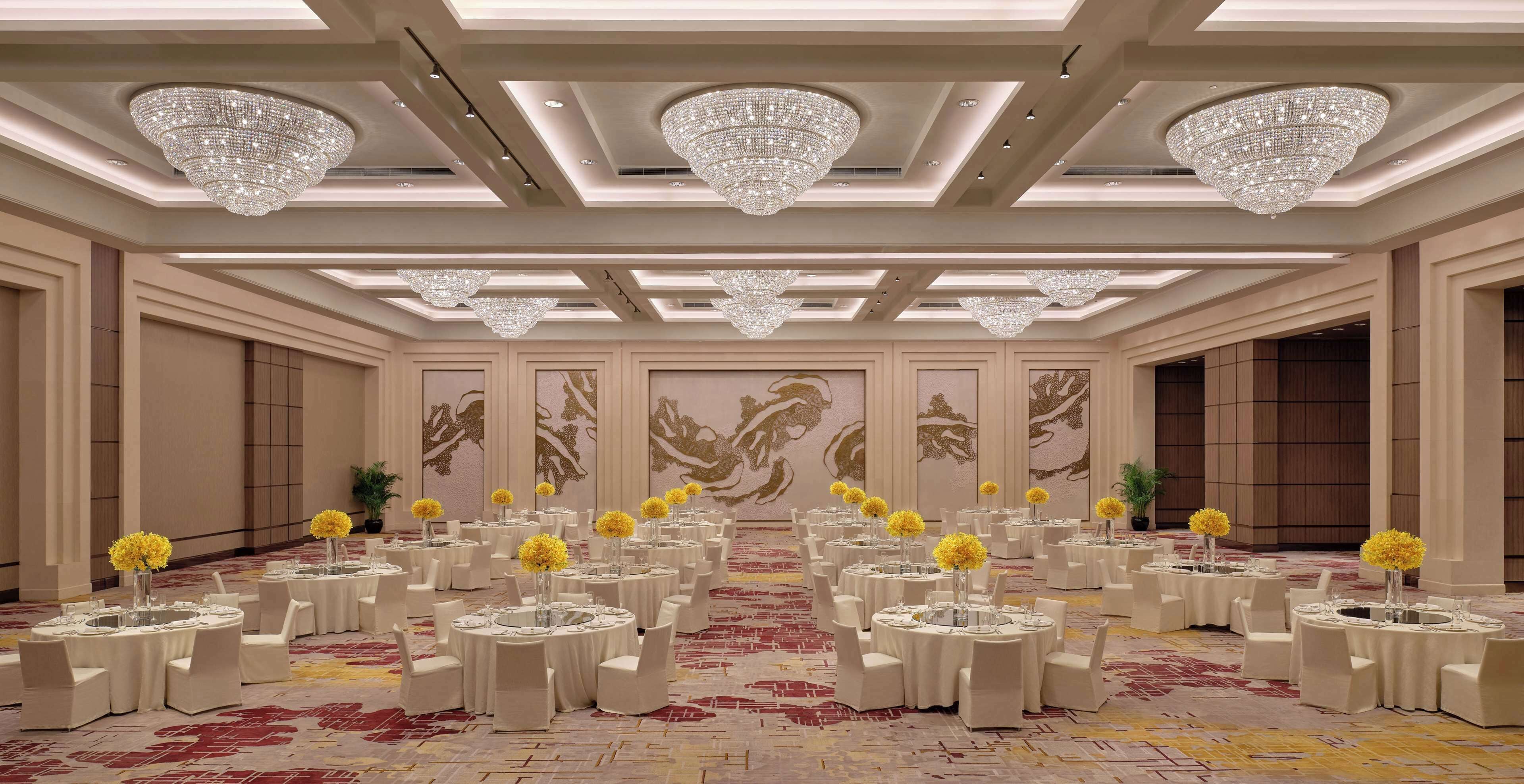 A banquet hall with round tables, white chairs, and chandeliers.