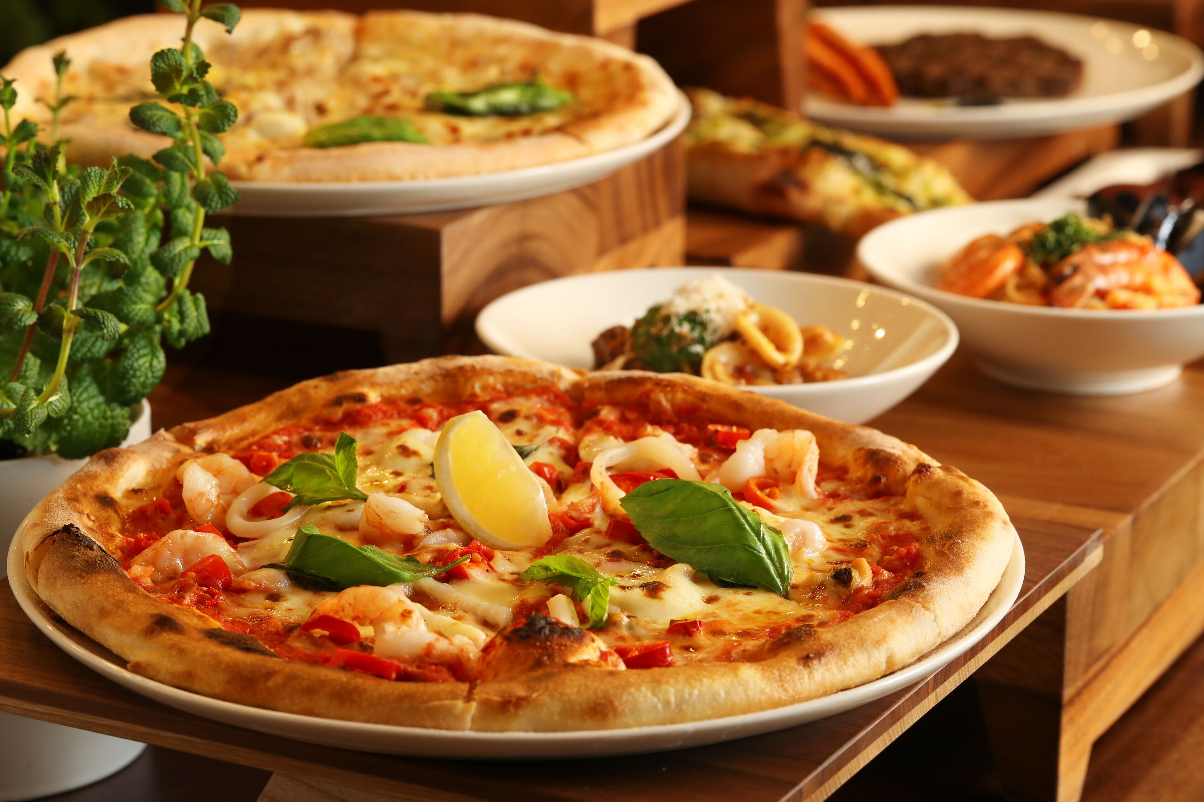 A pizza with shrimp, cheese, and basil on a wooden table.