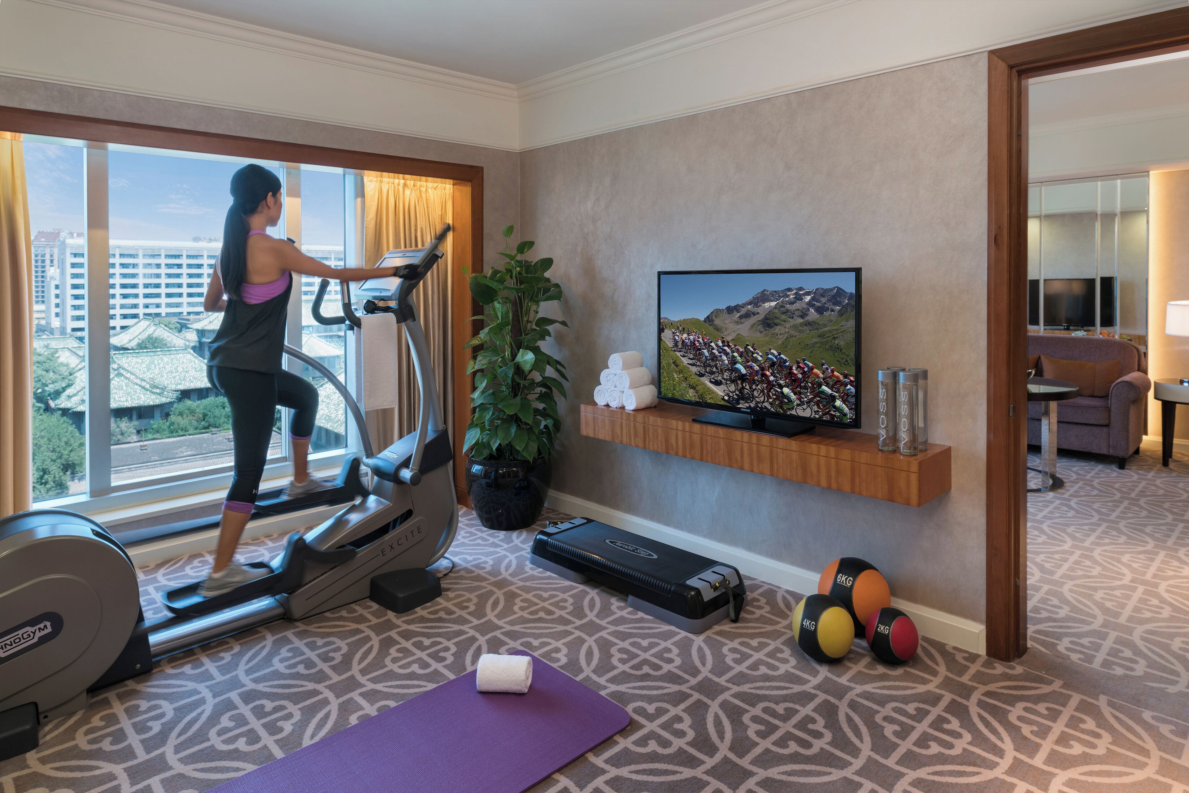 Habitación de hotel con una cinta de correr, televisor, pelotas de ejercicios y esterilla de yoga.