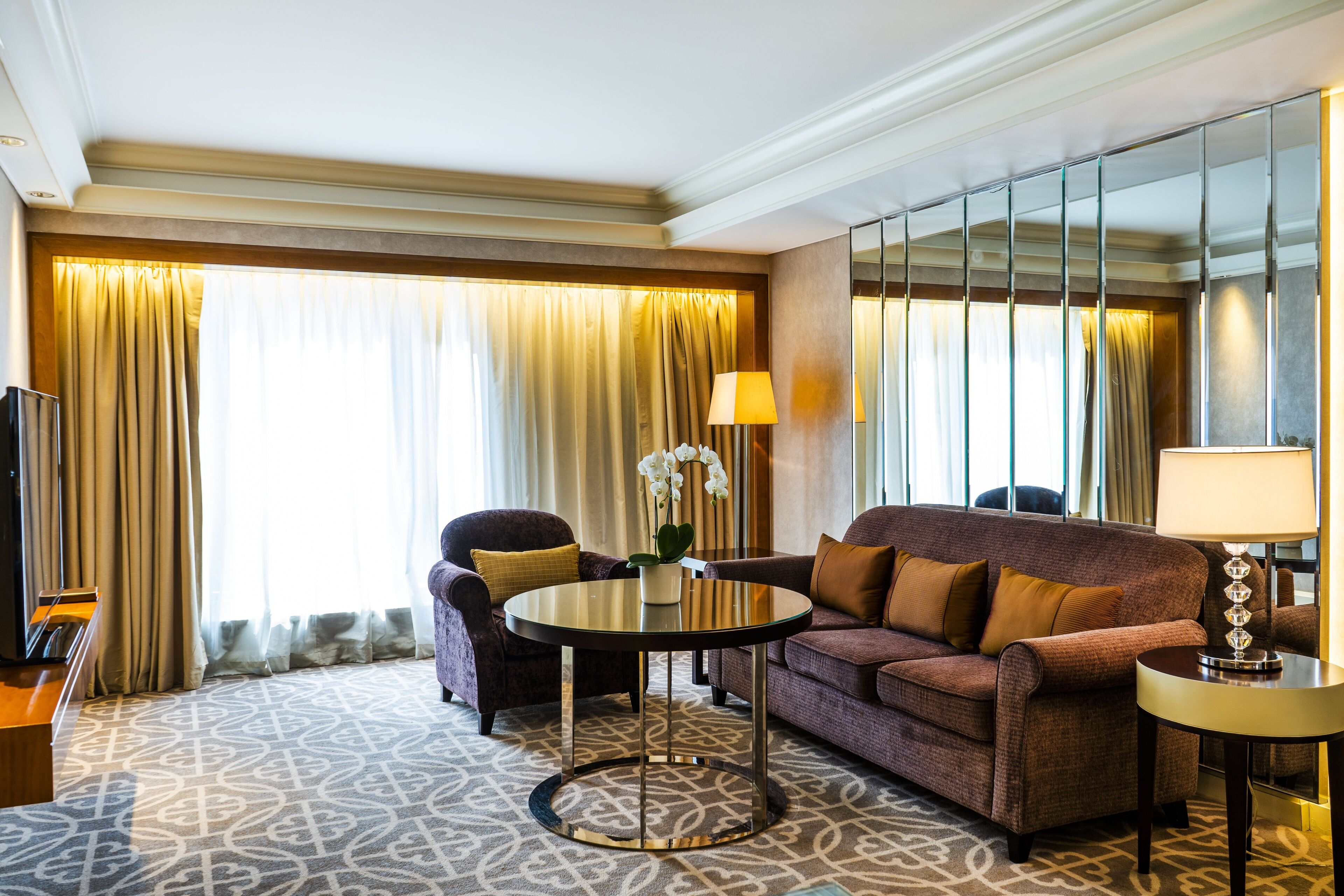 A hotel room with a sofa, armchair, round coffee table, and a TV.