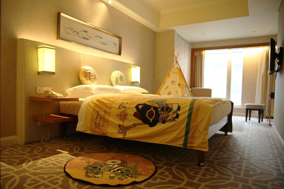 A hotel room with a bed, bedside table, lamp, and a window with curtains.