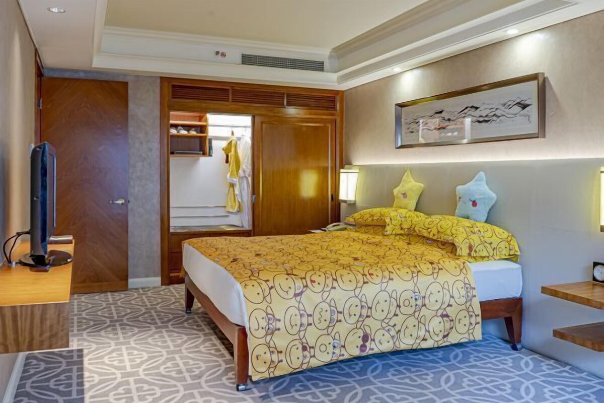 A hotel room with a bed, a TV, a wardrobe, and a painting on the wall.