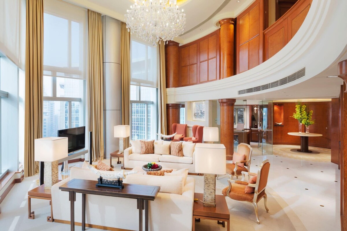 A spacious lobby with a high ceiling, large windows, a chandelier, and a seating area with a television.